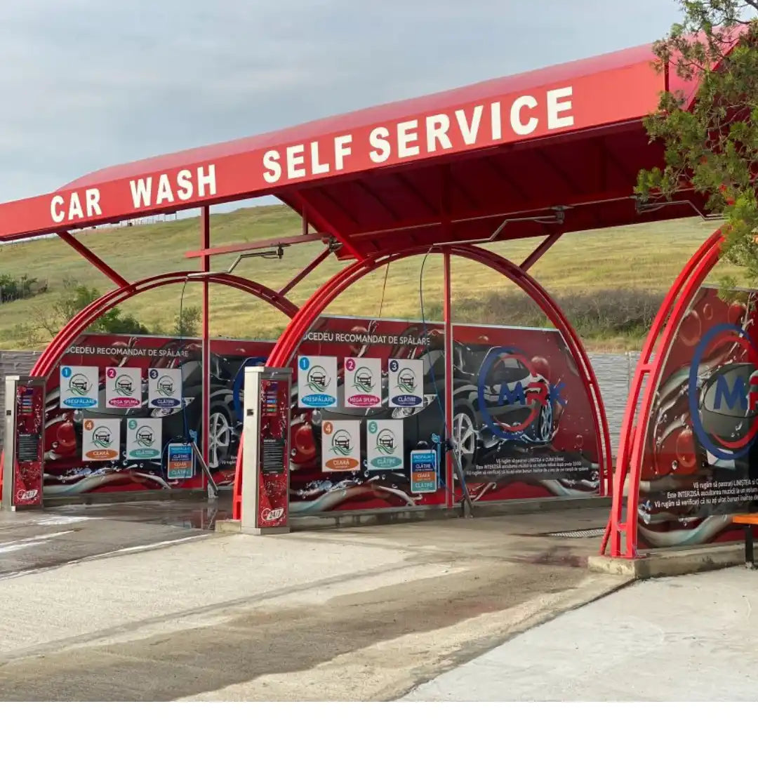 Stație de spălat auto self-service cu copertină roșie și multiple spații de spălare.